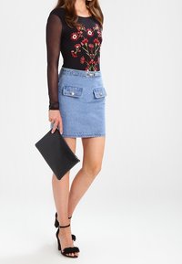 Schwarzes Langarmoberteil mit floralem Stickerei, hellblaue Jeansrock mit zwei vorderen Taschen, schwarze Clutch-Tasche und schwarze offene High Heels.