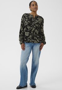 Blouse noire à motif de feuilles vertes, manches longues et patte de boutonnage; associée à un jean évasé bleu clair et des chaussures noires.