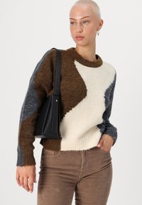 Pull en maille avec des sections marron, crème et gris présentant des motifs texturés. Associé à un pantalon en velours côtelé marron et un sac à bandoulière noir.