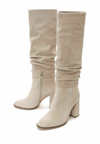 Stivali al ginocchio in suede beige con design a pieghe, punta quadrata e tacco spesso. Presentano una zip laterale per una facile indossabilità.
