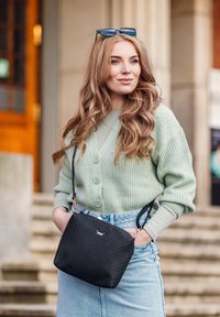 Světle zelený pletený kardigan se třemi knoflíky, přeložený přes světle zelený top. Džínová sukně s vysokým pasem. Černá prošívaná kabelka s logem.