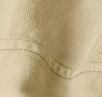 Tessuto a maglia beige con una trama testurizzata e cuciture visibili. Il tessuto è piegato, evidenziando la sua consistenza morbida e flessibilità.