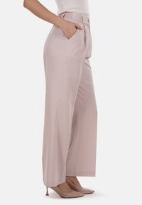 Pantaloni a gamba larga rosa chiaro con una texture liscia, dotati di tasche laterali e di una vita alta, abbinati a scarpe beige con punta a contrasto.