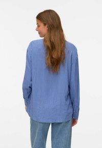 Blårandig långärmad skjorta med avslappnad passform, knäppta manschetter och mjuk textur. Backvy visar en rundad fåll. Lätta denimbyxor.