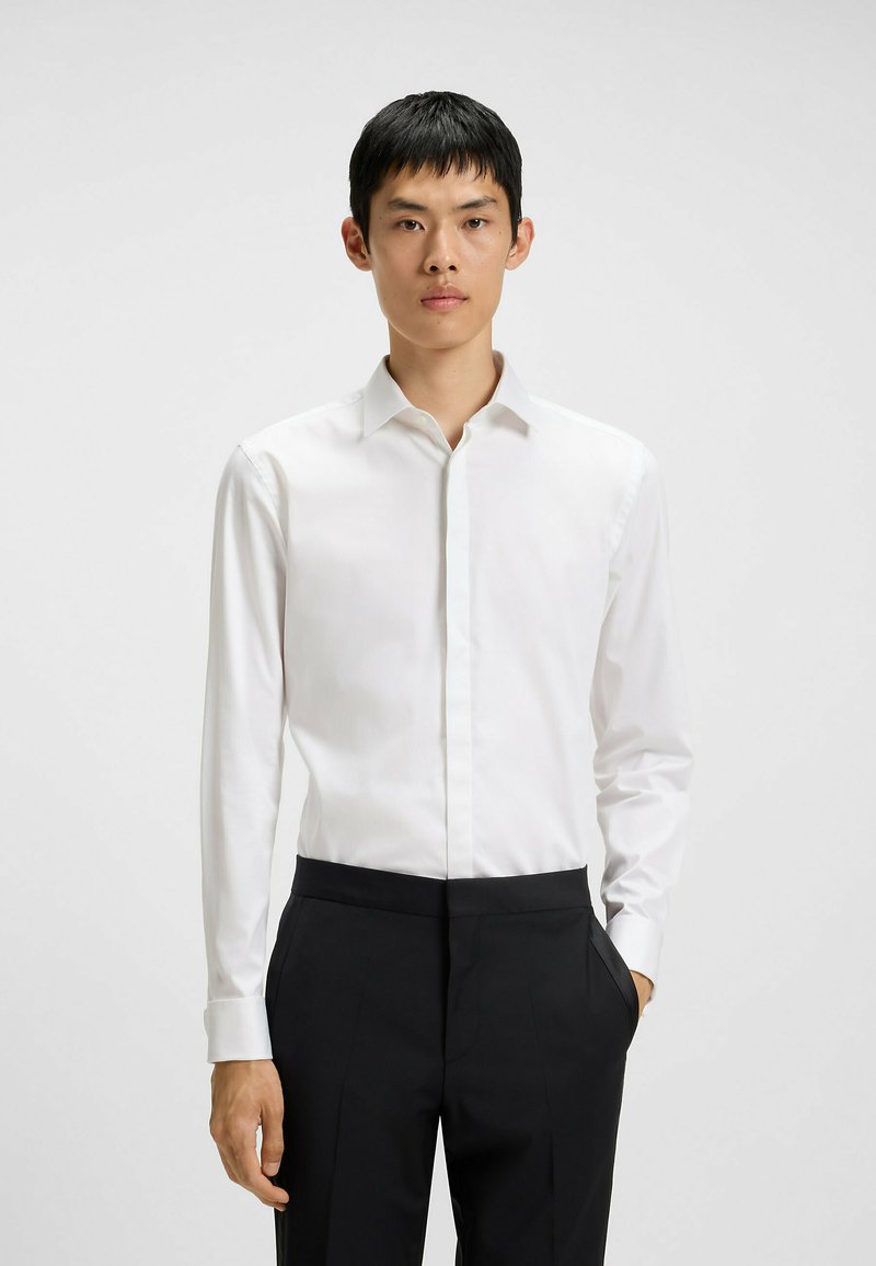 Witte langemouwenhemd met een puntige kraag, een gladde textuur en een knoopsluiting, gecombineerd met zwarte op maat gemaakte broek.