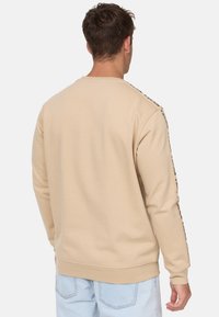 Sudadera beige con cuello redondo y mangas largas. Presenta detalles laterales en contraste y una tela suave y texturizada.