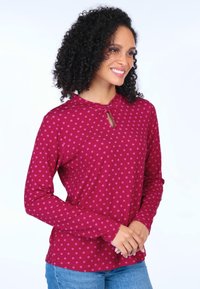 Langärmliges weinrotes Oberteil mit rosa Punkten, ausgestattet mit einem Schlüsselloch-Ausschnitt und aus weichem Stoff, kombiniert mit hellblauen Jeans.
