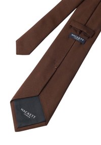 Cravate rayée marron avec une texture lisse. Elle possède une étiquette bleu foncé avec du texte blanc au bout. Design fin, extrémité pointue.