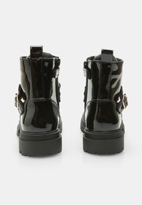 Botine din piele patent neagră, cu talpă groasă, având curele decorative și catarame pe laterale. Textură netedă și lucioasă.