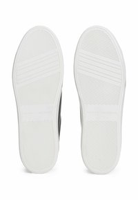 Ein Paar weiße Gummischuhsohlen mit diagonalen und horizontalen Rillen, auf denen "Tommy Hilfiger" in der Mitte eingestanzt ist.