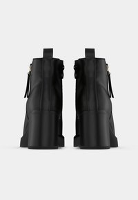 Crne gležnjače od umjetne kože s visokim blok petom, bočnim patentnim zatvaračima i glatkom teksturom. Imaju petlju za izvlačenje na stražnjoj strani.