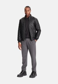 Chaqueta bomber negra acolchada con cuello alto, cierre de cremallera y puños de canalé, combinada con pantalones grises y botas negras con cordones.