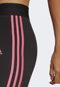 Svarta leggings med en bred svart midja och tre vertikala rosa ränder på sidan, tillverkade av ett slätt, elastiskt material.