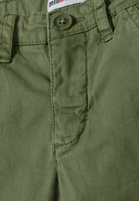 Pantalons en coton khaki avec une poche frontale, des coutures visibles et une fermeture à bouton. Texture douce avec une finition lisse et mate.