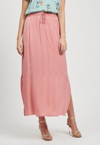 Jupe maxi rose avec une taille élastique et un cordon de serrage. Le tissu est léger avec une texture lisse. Les fentes latérales améliorent le mouvement.
