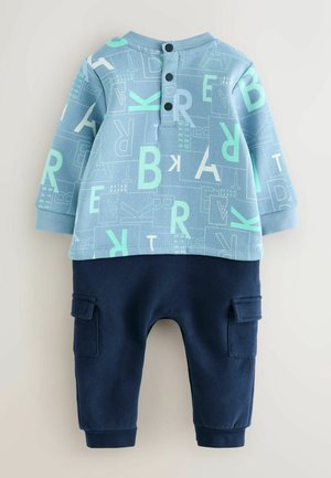 Helles blaues Langarmhemd mit abstraktem weißen und mintgrünen Druck, kombiniert mit dunkelblauen, gekrempelten Hosen mit Seitentaschen.