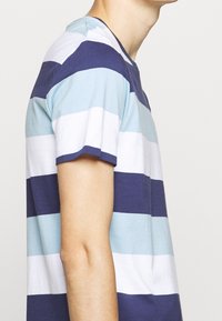 T-shirt a righe con bande orizzontali in azzurro chiaro, blu scuro e bianco, realizzato in morbido cotone, con colletto tondo e maniche corte.