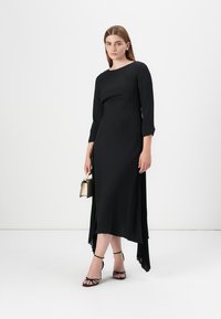 Black dress with a fitted bodice, three-quarter sleeves, and an asymmetric hem. Smooth texture with pleated accent at the back.