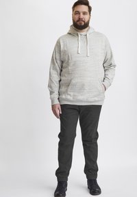 Lys grå, teksturert hettegenser med snor, foran lomme; kombinert med mørkegrønne bukser med elastisk mansjett og svarte snørebåndsstøvler.