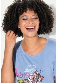 Camiseta de algodón de color azul claro con un estampado gráfico colorido que incluye el texto "be in" y un diseño floral. Cuello redondo y mangas cortas.