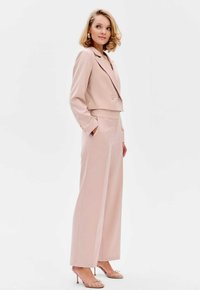 Lichtroze op maat gemaakte cropped blazer met dubbele knopen, gecombineerd met wijde broekspijpen met zijnaden. Glad stof met gepolijste accenten.