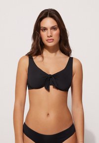 Schwarzer Bikini-Oberteil aus glattem Stoff, mit einem Knoten-Detail vorne und breiten Trägern, ergänzt durch ein einfaches Design mit klassischer Silhouette.
