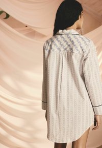 Pitkähiha maiho kevyestä kankaasta, jossa on sininen kukkakuosi pääntiellä, pystysuorat striippikuviot ja mustat reunukset hihansuissa.