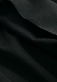 Tissu noir avec une texture lisse, présentant des plis subtils et une légère brillance. Le matériau semble doux et légèrement élastique.