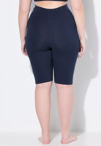 Námořnické vysoké cyklistické šortky vyrobené z měkké tkaniny, s hladkým pasem, přiléhavým střihem a délce ke kolenům. Bez viditelných vzorů nebo akcentů.