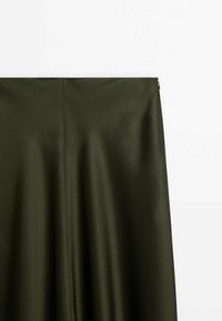 Jupe vert foncé avec une texture de tissu lisse, présentant une couture au centre et une petite fermeture éclair en haut à droite.