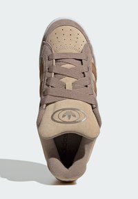 Tan ruskinds sneakers med brune detaljer, perforeret tå, teksturerede snørebånd og et rundt logo på tungen. Hvid ydersål for kontrast.