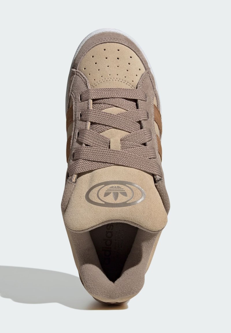 Sneaker in suede tan con dettagli marroni, punta perforata, lacci texture e un logo circolare sulla linguetta. Suola bianca per contrasto.