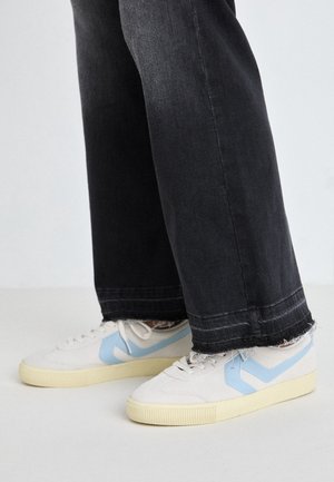 Zapatillas blancas con acentos en azul claro, tela texturizada y suelas de goma amarilla. Combinadas con jeans anchos desgastados en negro.