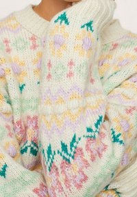 Pull en maille épaisse crème avec des motifs floraux et géométriques multicolores. Détails comprenant des poignets côtelés et un large décolleté.