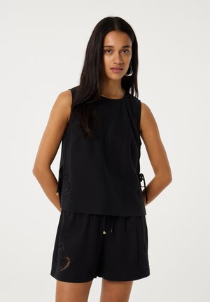 Zwarte mouwloze top met een ontspannen pasvorm, met zijdrawstrings en ingewikkelde hartpatroonaccenten aan de zoom. Gecombineerd met bijpassende shorts.