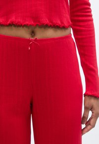 Ensemble de vêtements d'intérieur côtelé rouge comprenant un haut court aux bords effilochés et un pantalon assorti à taille nouée. Tissu doux en mélange de coton.