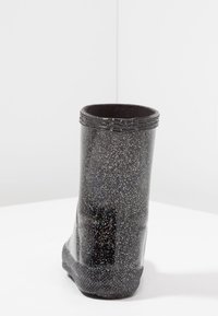 Bota negra impermeable con un acabado brillante, que presenta manchas plateadas, un borde superior texturizado y una suela antideslizante para mayor estabilidad.