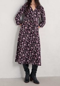 Czarna sukienka w kwiaty z długimi rękawami, z różyczkowym nadrukiem w odcieniach różu i bieli, z przylegającą talią i falującym dołem, połączona z wysokimi czarnymi botkami.