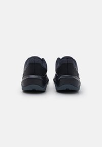 Sorteidrettssko med teksturert overdel, avrundet hæl og polstret såle. Har minimal merkevare og et glatt, strømlinjeformet design.