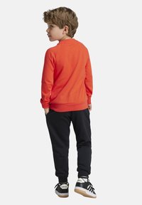 Sudadera roja de manga larga con cuello redondo, combinada con pantalones negros y zapatillas negras con rayas blancas y suelas de goma.
