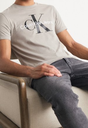 T-shirt en coton gris avec un graphisme noir "Calvin Klein Jeans", à manches courtes et coupe ajustée, assorti à un jean gris foncé.