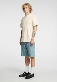 Beež värvi lühikeste varrukatega T-särk, lõdva lõikega, kombineeritud helesiniste teksapükstega ja mustade loafers-tossudega, kantud valgete pahkluu sokkidega.