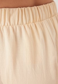 Lichtbeige stof met een elastische tailleband, met een geplooide textuur en een zachte, gladde oppervlakte. Geschikt voor casual wear.