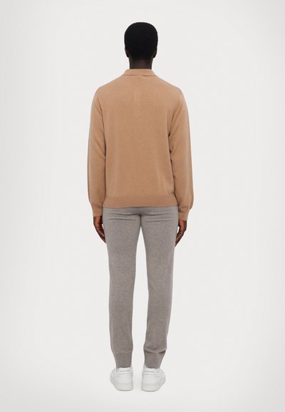 Beige kötött pulóver gallérral, világosszürke, tapered fazonú nadrággal párosítva. Az öltözetet fehér sneakers lábbeli egészíti ki. Egyszerű és texturált anyagok.
