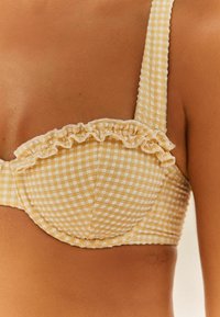 Gul gingham-bh med volangdetaljer, rutigt mönster och breda band, tillverkad av texturerat tyg. Böjda kupor ger strukturerat stöd.