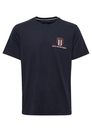Tumši zils kokvilnas t-krekls ar īsām piedurknēm un apaļu kaklu. Ar izšūtu vairoga logotipu, kas satur tekstu "1924" un "HIGH PERFORMANCE".