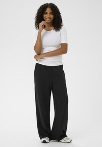 Hvid tætsiddende skjorte med korte ærmer, parret med sorte vide bukser og cremefarvede sneakers. Enkelt design med en glat overflade.