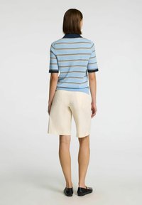 Světle modrá pruhovaná polo košile s krátkým rukávem, tmavomodrý límec, doplněná béžovými kraťasy ke kolenům a černými plochými botami.