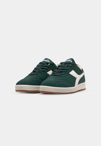 Green suede sneakers with white accents, round toe, and flat rubber sole. Features traditional lace-up design and cushioned collar.