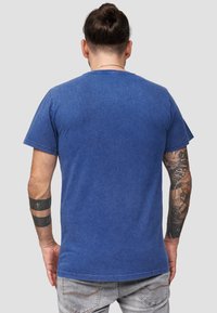 Blå bomullströja med kort  ärm, med rund hals och en något blekt textur. Synliga tatueringar på armen.